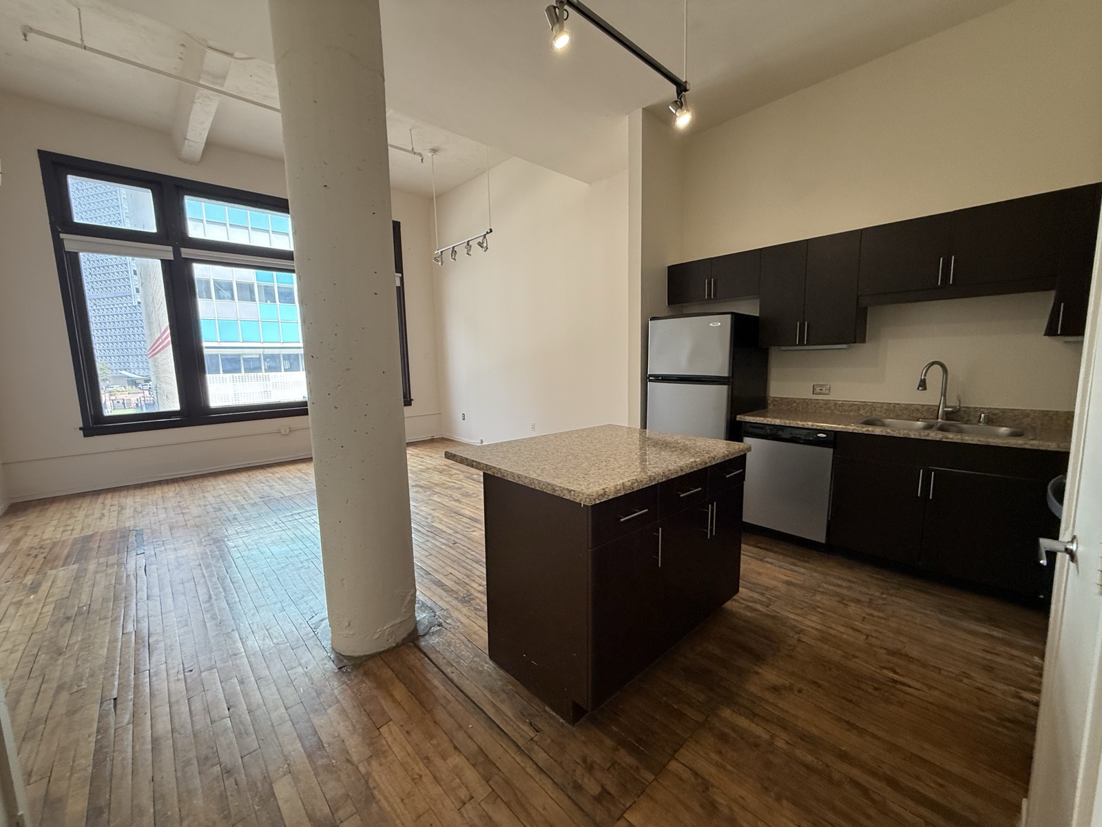 The open kitchen and dining area — granite island, full cabinets, sink and fridge, with windows onto downtown