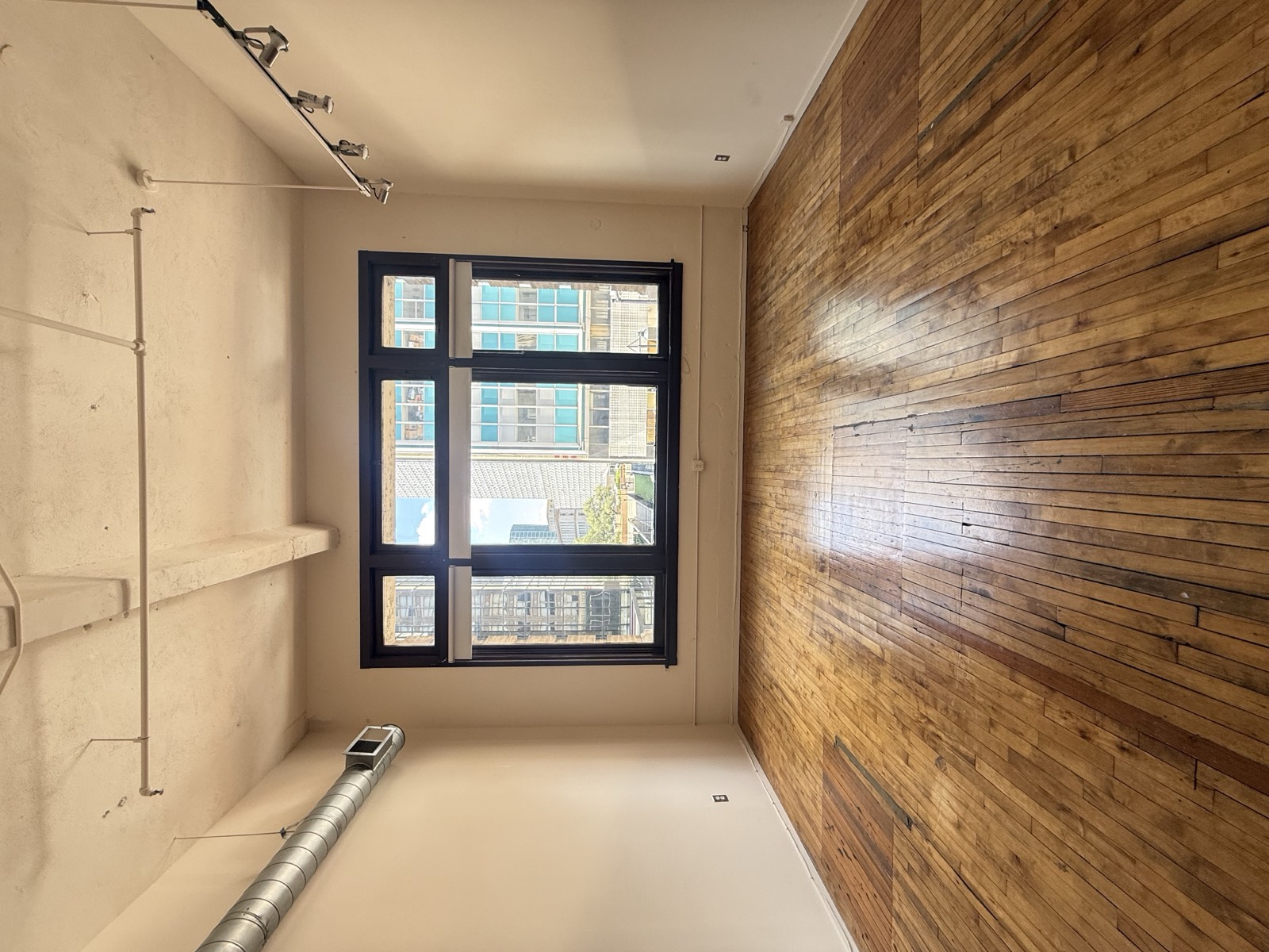 The same main room cleared out — bare hardwood floors, big windows, and track lighting