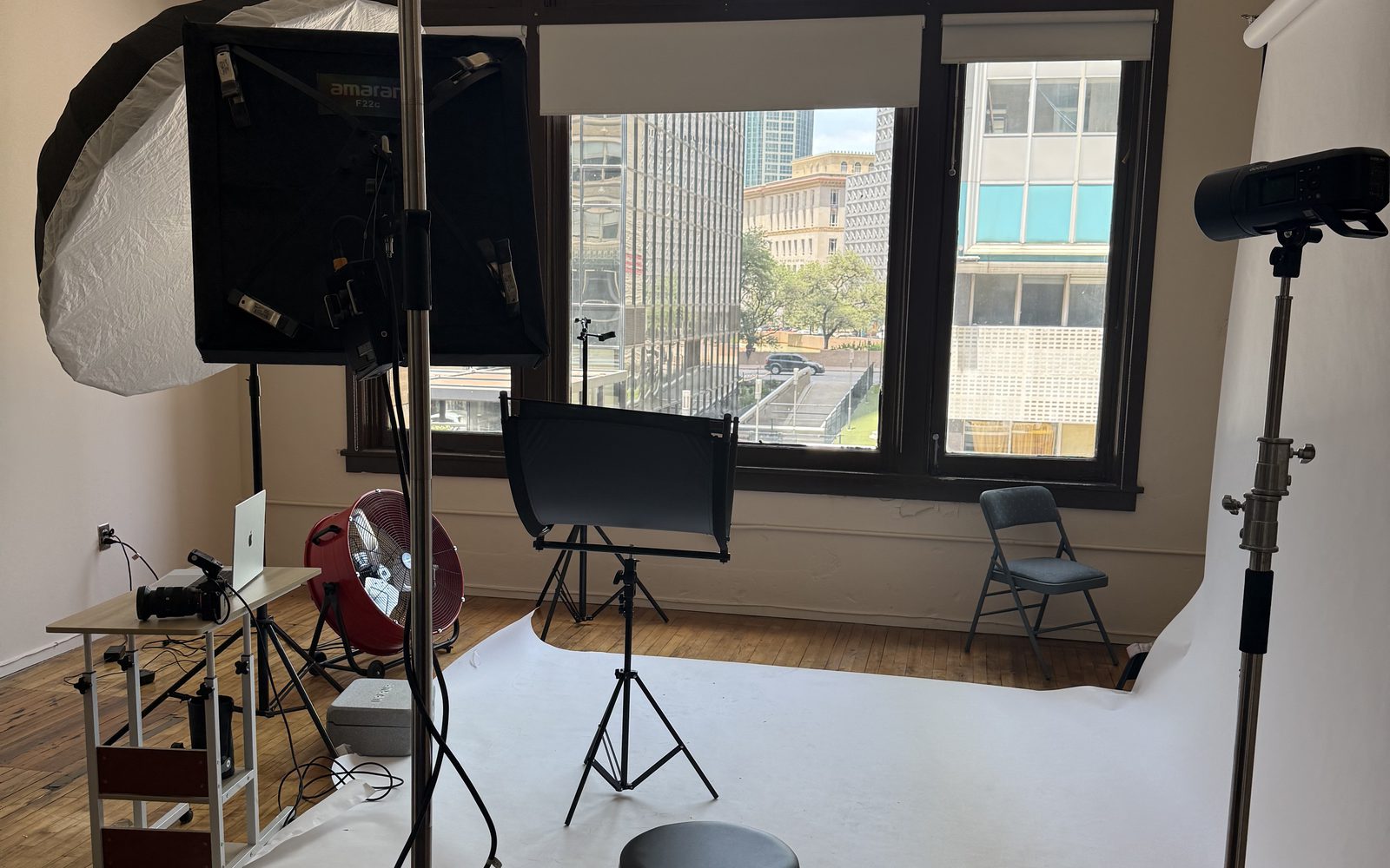 Jenel Studios set up for a shoot: a white backdrop on the hardwood floor, lights on stands, and big windows onto downtown Dallas