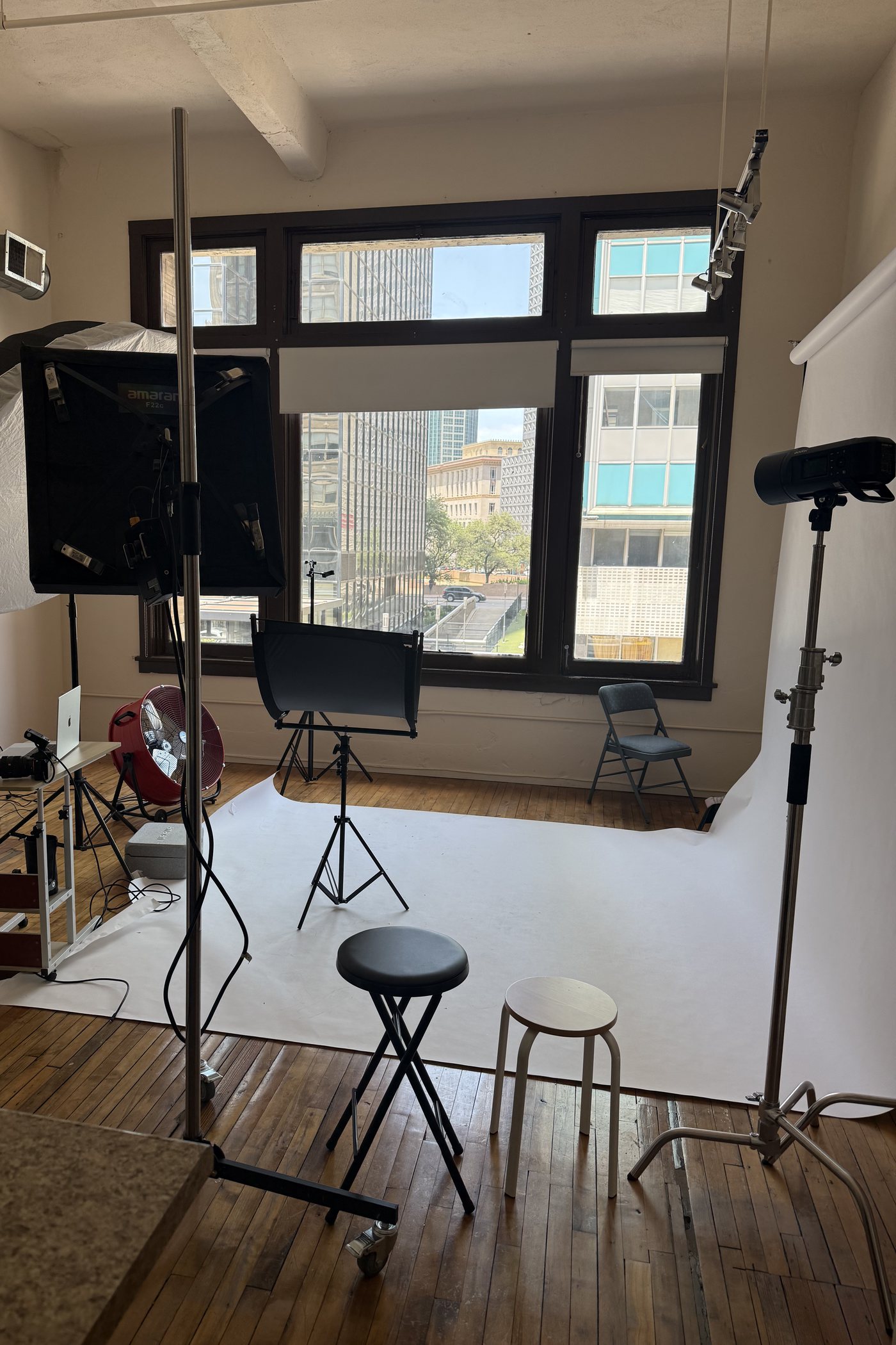 The studio mid-shoot — a white backdrop swept across the hardwood, lights and stands set up, and downtown Dallas through the windows